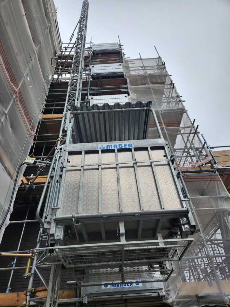 Lift de chantier MABER MBC 1000 vu depuis le pied du mât, le long d'un échafaudage de façade