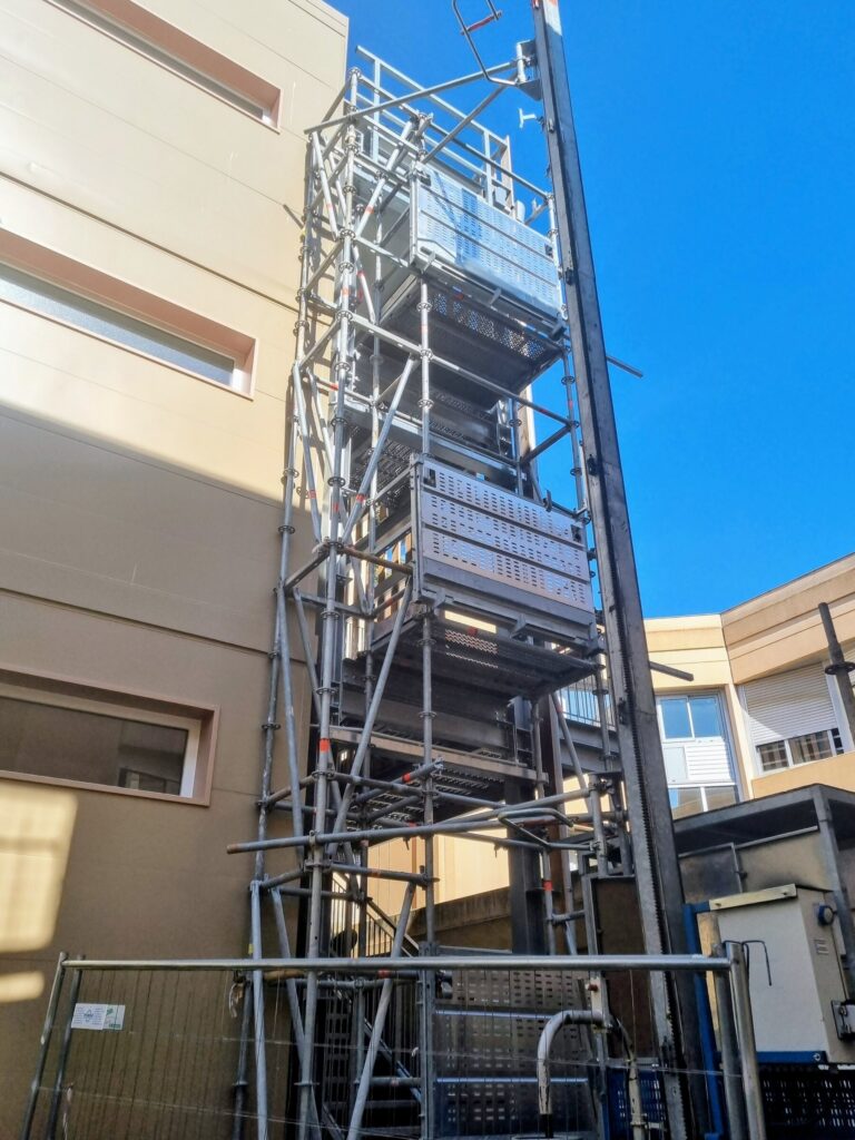 Lift de chantier MABER monté contre une tour escaliers d'échafaudage, un palier d'accès à chaque niveau