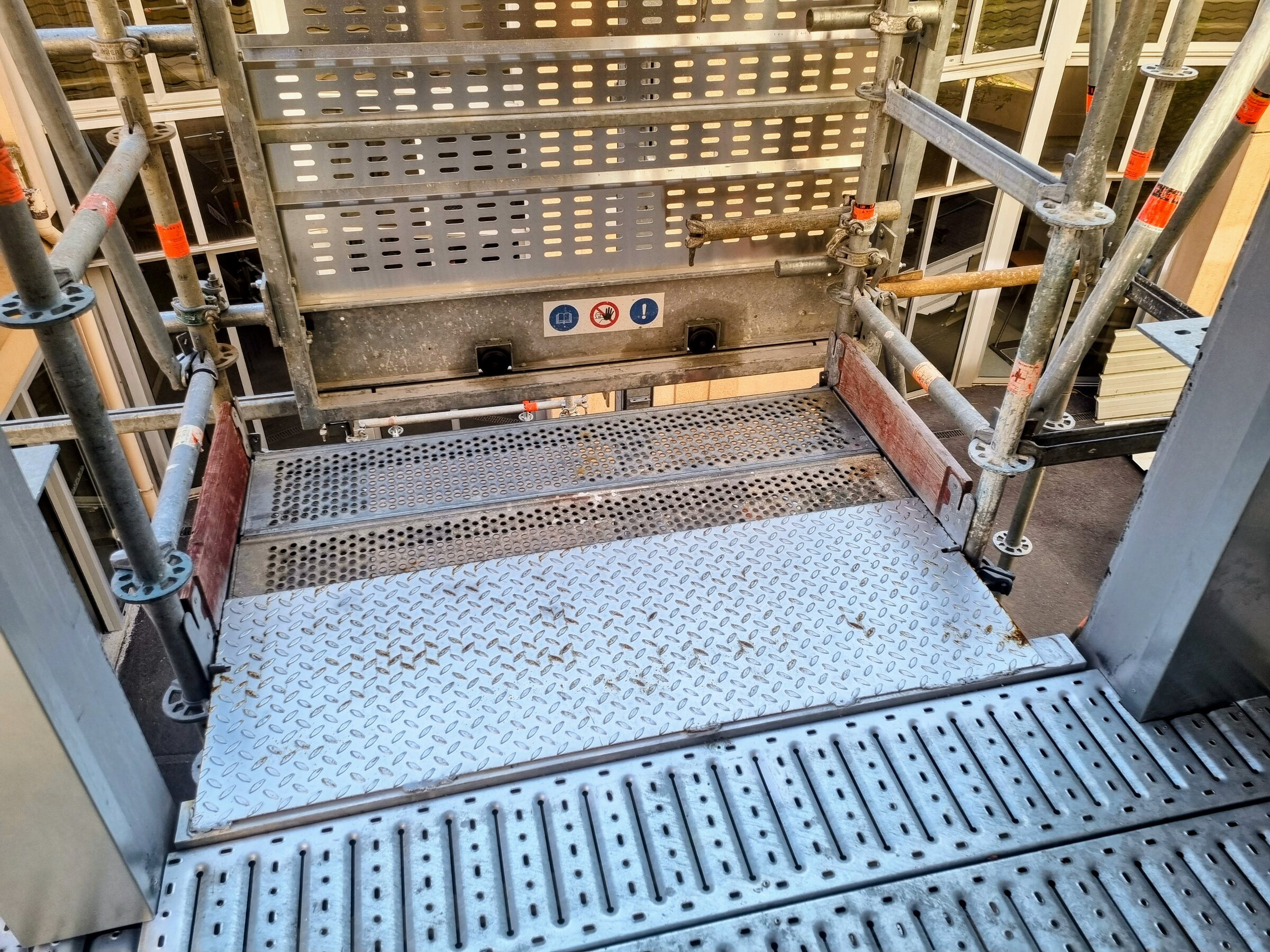 Plateau d'un lift de chantier MABER MBC 500 arrivé au palier d'un échafaudage, rampe en tôle et garde-corps
